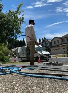 Professional exterior cleaning technician pressure washing a residential driveway in Folsom, California, with a Wash Works service van in the background.