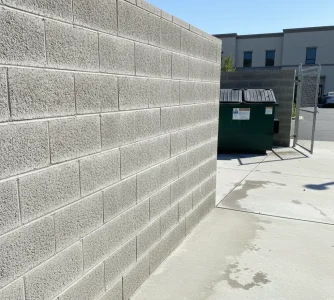 Clean concrete dumpster pad area next to a block wall at a commercial building in Sacramento after professional pressure washing service