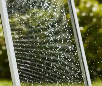 Close-up of a window screen being cleaned with water spray outdoors in Fair Oaks, showcasing expert exterior screen washing service.